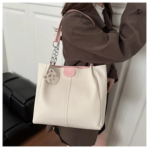 Detail of off-white tote bag with pink handles, metal chain straps and cartoon charm