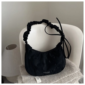 Detail of black pleated croissant bag with bow ribbon and fashion text on soft fabric