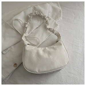 Detail of white pleated shoulder bag featuring elegant ruched strap texture design