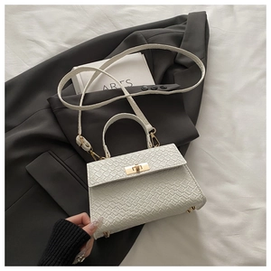 Détail d'un sac à main blanc à motif crocodile avec fermoir doré sur fond de blazer gris