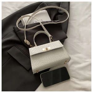 Gros plan d'un sac à main blanc tressé avec fermoir doré à côté d'un smartphone