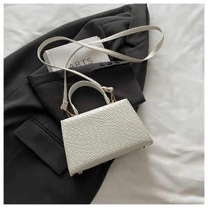 Détail d'un mini sac à main blanc motif crocodile avec pieds dorés sur fond chic