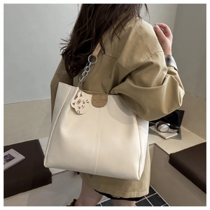 Detail of a beige tote bag with a tiger charm and leather tag in a cafe setting