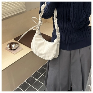 White shoulder bag featuring ruffled straps and bow tie detail in a lifestyle setting