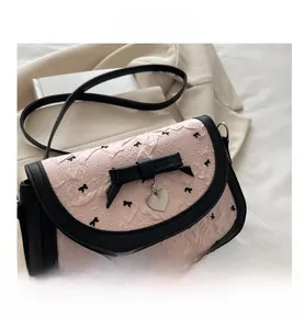 Détail du sac bandoulière rose à motif nœuds avec bordure en cuir et pendentif cœur