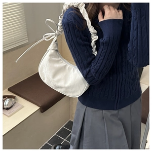 Detail of white pleated shoulder strap and leather bow on this hobo dumpling bag