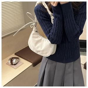 Detail of white pleated crescent bag featuring a stylish bow knot on the strap