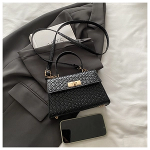 Détail d'un sac à main noir tressé avec fermoir doré et pieds de protection en métal