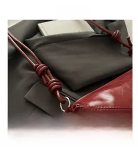 Detail of dark red glossy tote bag featuring a stylish knotted strap and silver ring buckle