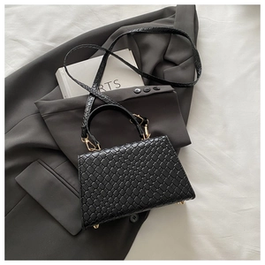 Détail d'un sac à main en cuir tressé noir montrant la texture sur une veste grise