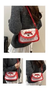 Détail du sac bandoulière rouge et blanc avec imprimés nœuds et pendentif cœur argenté