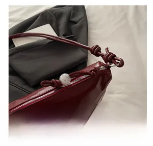 Detailed close-up of dark red glossy half-moon tote bag with pearl charm and silver zipper