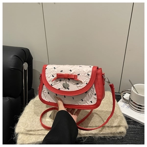 Détail d'un petit sac bandoulière avec texture plissée blanche, nœud rouge et pendentif