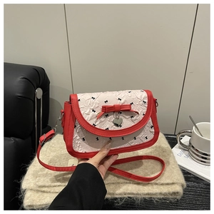 Détail du sac crème avec bordure rouge, nœuds floraux et pendentif en forme de cœur argenté