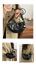Detailed macro view of black glossy crescent bag with knot straps and pearl charm