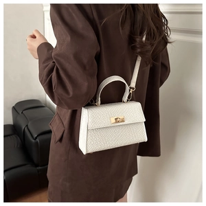 Détail du sac à main blanc motif crocodile avec fermoir doré sur un manteau marron