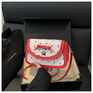 Détail d'un sac à fleurs matelassé avec nœud rouge et breloque cœur dans un coffret