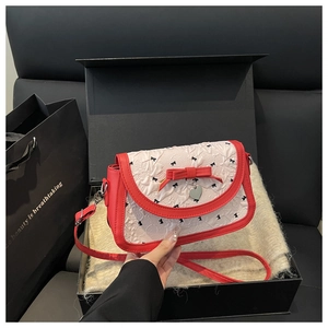 Détail du sac bandoulière en cuir rouge avec rabat brodé blanc dans un coffret cadeau