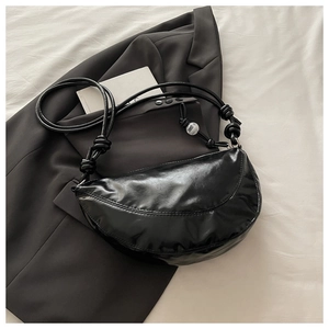 Vue détaillée du sac demi-lune en cuir brillant noir avec bandoulière à nœud et bille