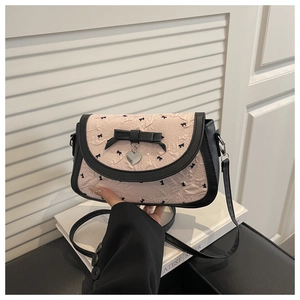 Détail du sac bandoulière rose plissé avec nœud noir et pendentif cœur argenté élégant