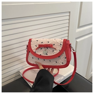 Détail d'un sac rouge en cuir avec rabat plissé crème et pendentif en métal cœur