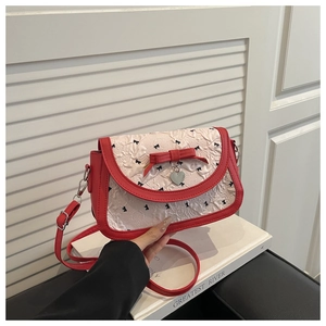 Détail du sac à bandoulière rouge et blanc avec nœud, pendentif cœur et tissu plissé
