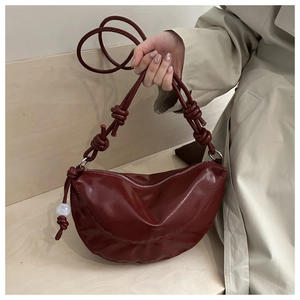 Détail du sac demi-lune verni bordeaux avec bandoulière nouée et perle décorative