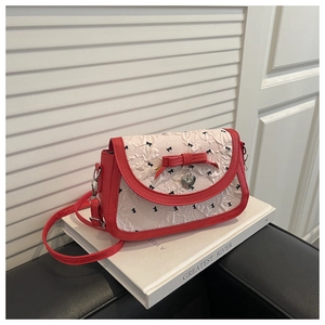 Détail du sac en cuir rouge avec tissu plissé blanc et motifs de nœuds brodés noirs