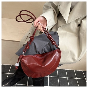 Détail du sac demi-lune rouge foncé avec bandoulière nouée et pendentif sphérique poli
