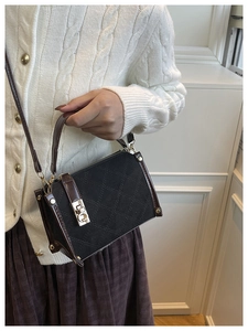 Detail of black quilted box bag with gold hardware and brown leather shoulder strap