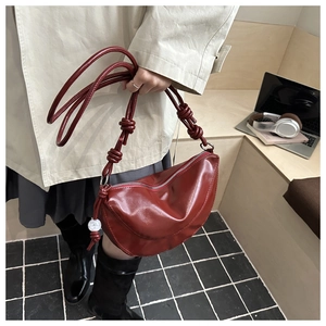 Detail of dark red crescent bag with knotted strap and polished leather texture