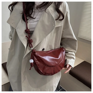 Détail du sac triangle en cuir souple bordeaux avec bandoulière nouée et pompon blanc