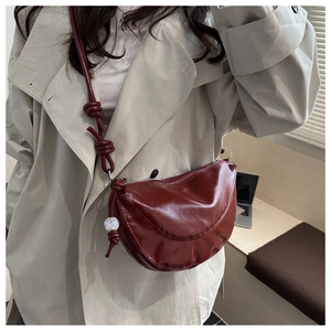 Detail of dark red crescent bag featuring knotted strap and marble bead accessory