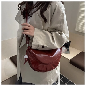Détail d'un sac demi-lune bordeaux avec bandoulière nouée et perle décorative unique