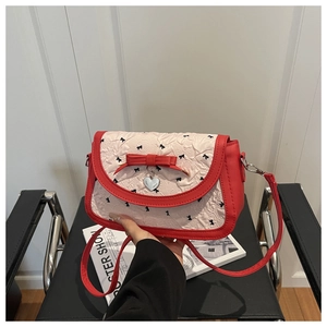 Détail du sac à bandoulière en cuir rouge avec nœuds noirs et pendentif cœur argenté