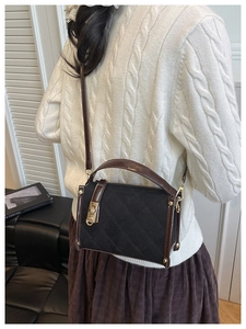 Detail of the black quilted small square bag with brown leather trim and gold metal buckle