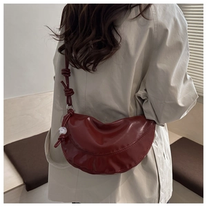 Détail du sac croissant bordeaux avec bandoulière nouée et pendentif sur trench beige