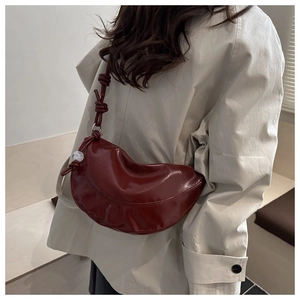 Détail du sac lune bordeaux avec sangle nouée et perle sur un trench-coat beige