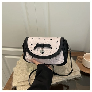 Détail d'un sac à motif nœuds roses avec un grand nœud noir et pendentif cœur argenté