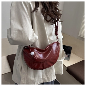 Détail macro du sac demi-lune bordeaux avec sangle nouée et bouton décoratif blanc