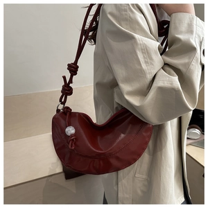 Détail d'un sac demi-lune bordeaux avec bandoulière nouée et perle sur un trench-coat