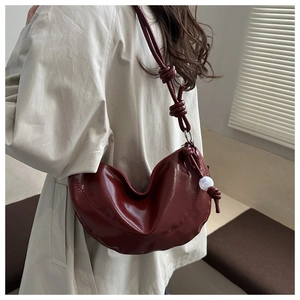 Détail du sac demi-lune bordeaux avec bandoulière nouée et breloque perle sur modèle