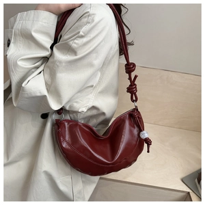 Détail du sac dumpling bordeaux avec bandoulière nouée et perle sur trench-coat beige clair