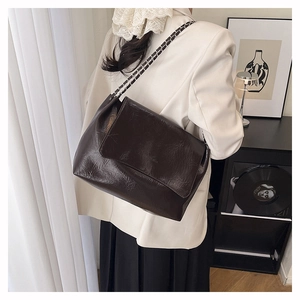 Detail view of deep brown oily wax texture and metal chain strap on minimalist handbag