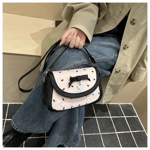 Détail d'un sac bandoulière rose à motif nœud avec pendentif cœur tenu à la main
