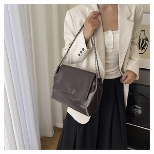 Detail of glossy chocolate brown shoulder bag with silver chain strap on model
