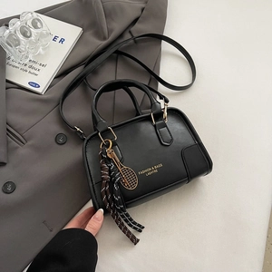 Black leather Boston handbag with gold tennis racket charm and woven tassel on gray blazer