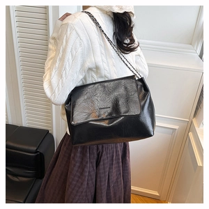 Macro detail of glossy pleated black PU leather bag with silver chain strap on model