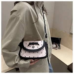 Détail du sac à bandoulière rose avec nœud et pendentif cœur sur une tenue beige