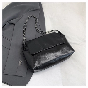 Détail du sac noir à plis en similicuir avec bandoulière chaîne et texture brillante